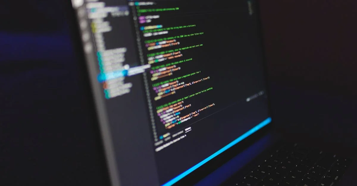 Ordinateur portable affichant du code dans un environnement sombre, mettant en avant des concepts de programmation et le travail numérique.