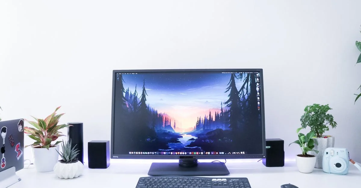 Bureau contemporain présentant un moniteur, des plantes et des appareils électroniques dans un design épuré et minimaliste.