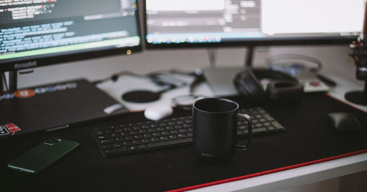Bureau à domicile confortable avec des écrans doubles, un clavier et une tasse en céramique noire.