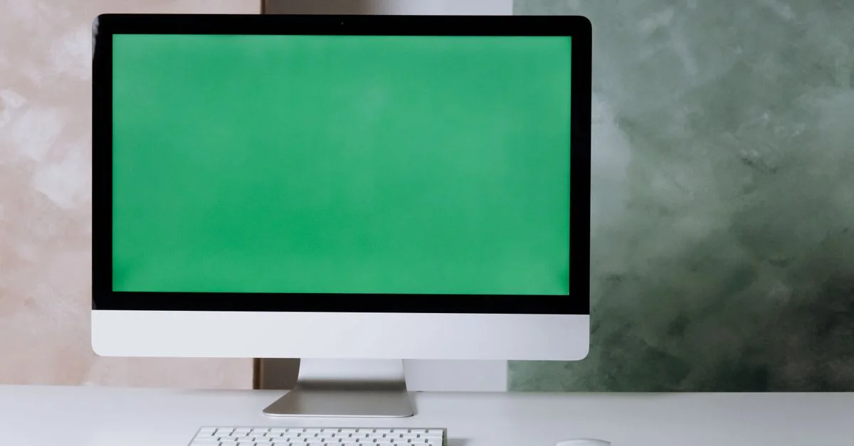 Configuration propre et minimaliste avec un ordinateur et un écran vert sur un bureau blanc.
