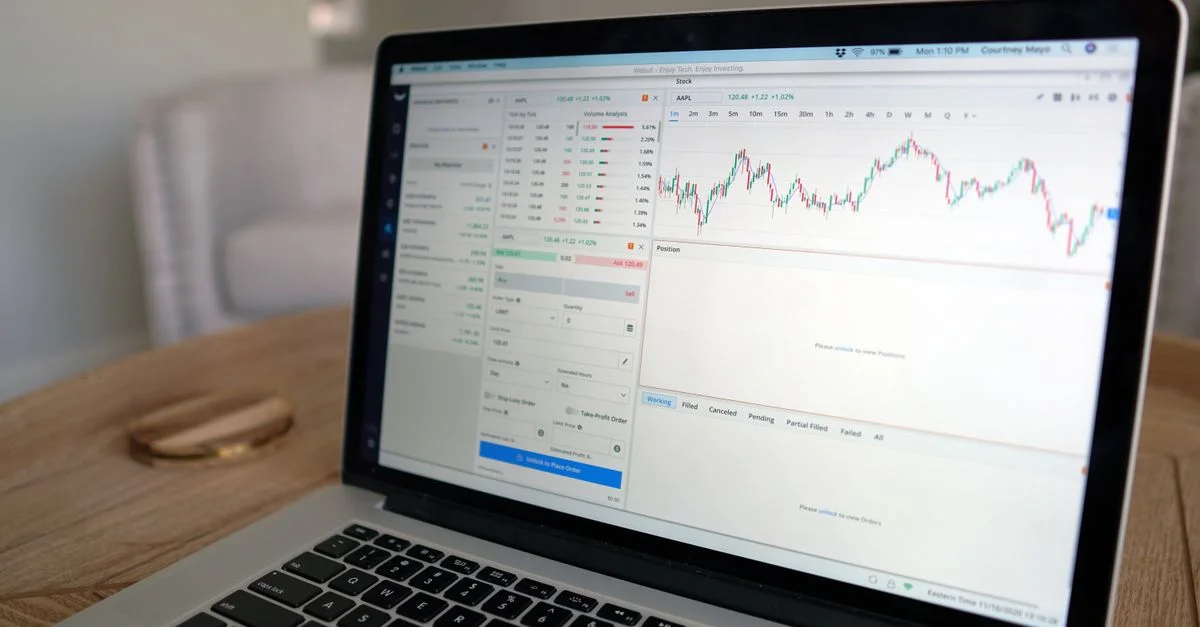 Gros plan d'un ordinateur portable affichant un logiciel de trading avec un graphique du marché sur une table en bois.