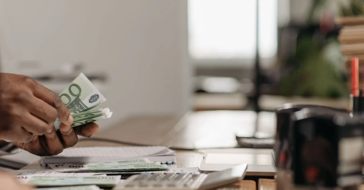 Gros plan de mains comptant des billets en euros sur un bureau de bureau avec une calculatrice.