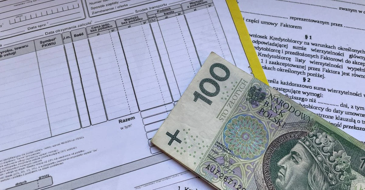Un billet de 100 zlotys polonais posé sur des documents financiers et des factures, sur le bureau.