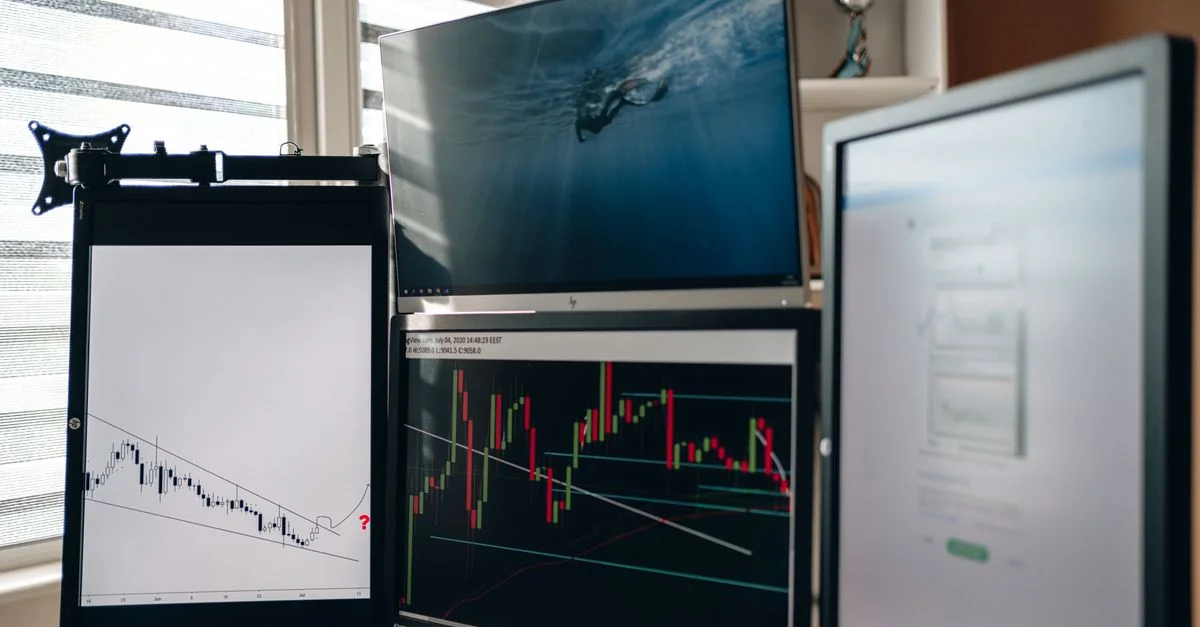 Un bureau à domicile avec plusieurs moniteurs affichant des graphiques de trading et des analyses de données.